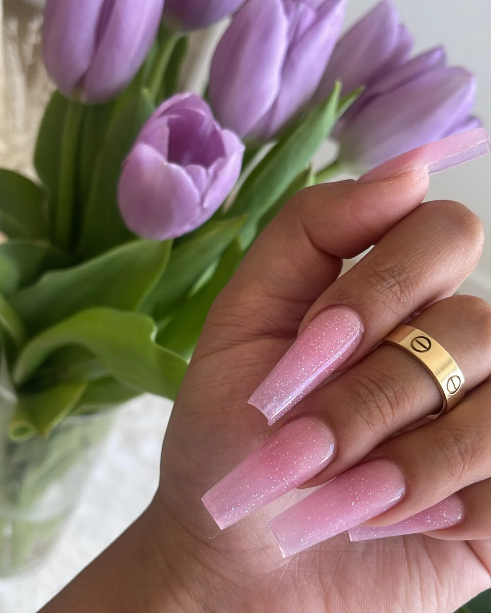 Soft pink glitter nails photographed with purple tulips