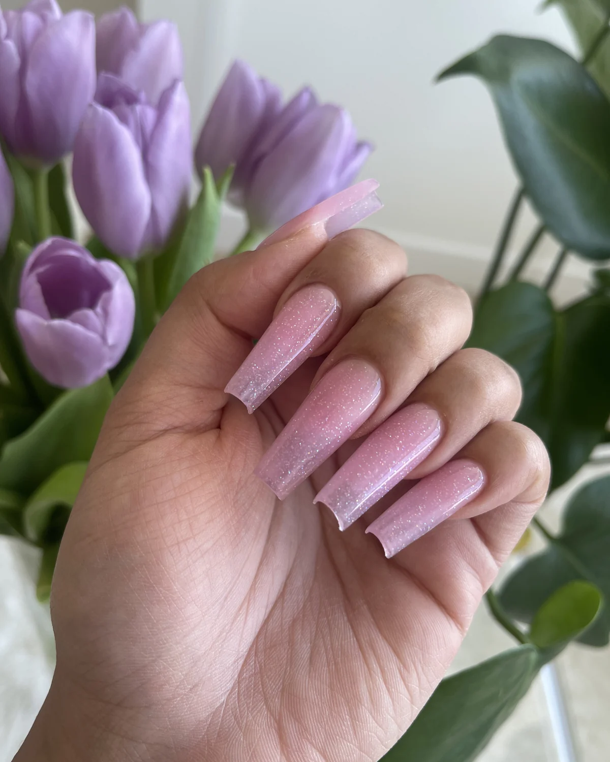 Soft pink glitter nail extensions photographed with purple tulips